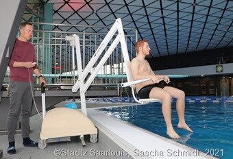 Mit dem mobilen Schwimmbadlift ist es problemlos möglich, Menschen mit Handicap vom Beckenrand ins Wasser zu lassen und sie wieder aus dem Wasser herauszuheben, wie es Betriebsleiter Thorsten Laurent mit Azubi Niklas Schmidt vorführt. Fotos: Sascha Schmidt