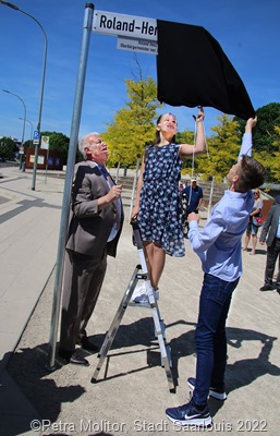 Oberbürgermeister Peter Demmer, Katharina und Sebastian Henz bei der Enthüllung des Schildes, das nun den „Roland-Henz-Platz“ kennzeichnet. 3091